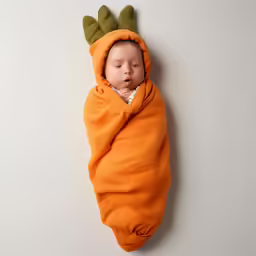 a baby sleeping in a blanket wrapped in a orange creature costume