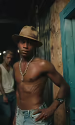 a man in a tan hat and jean shorts poses in an alleyway