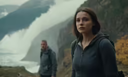 two people standing in the wilderness with mountains in the background