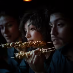 a woman sticks hot sauce on skewers with a man in the background