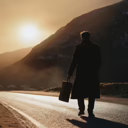 the man is holding a suit case and walking on the road