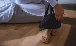 the woman is carrying her purse while standing near a bed