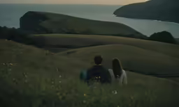 a couple siting in the grass by the water