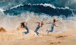 three girls jump up in the air over a sandy beach