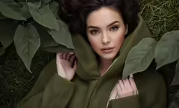 a beautiful woman laying in the grass under some leaves