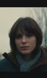 a woman in a blue and brown coat standing next to some trees