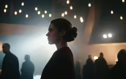 a girl looks to her right with blurry lights hanging overhead