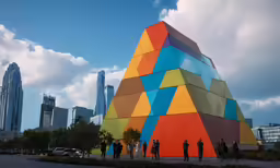 colorful sculpture surrounded by other large buildings on top of a hill