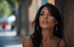 a woman is wearing big gold earrings standing near the tree