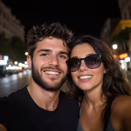 two people posing for a photo on a street at night