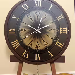 a large black clock with roman numerals,an analog clock with roman numerals on a table