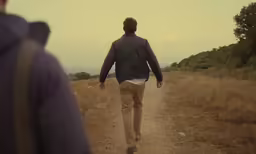 a man walks down a dirt road holding an umbrella