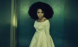 a black woman in a white dress stands in a dark room