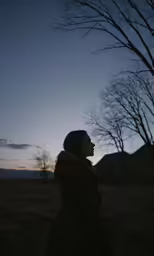 a woman is staring into the sky with a tree behind her