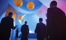 a group of people standing in a room with lights hanging from the ceiling