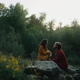 two people sitting together in the middle of a wooded area
