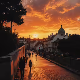 the sun sets on a cobblestone street with lots of people walking down it