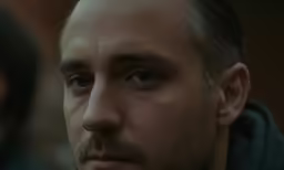 a man in a green jacket stares into the camera