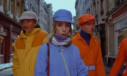 three people with orange and blue coats on are walking on a street