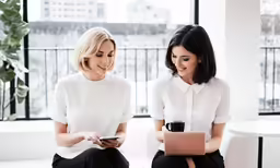 two female employees sit near each other, working with computers and tablet
