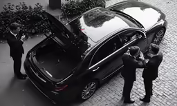 four people stand around a black car on a cobblestone street