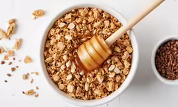 a wooden spoon pouring honey into a bowl of granola