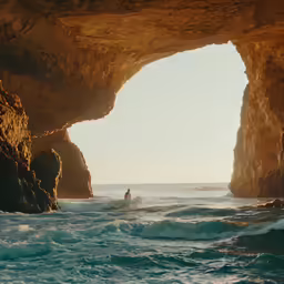 a person surfing in the ocean next to large rocks