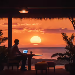 man working on laptop computer while sitting at a table overlooking the ocean