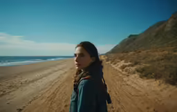 there is a woman in a blue jacket standing on the beach