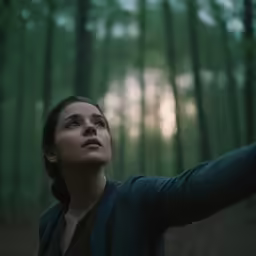 the woman is looking upward into the forest
