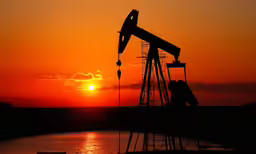 the sun rising over an oil rig by the water