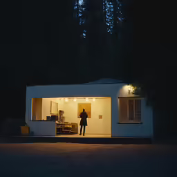 person standing in door way of white house at night