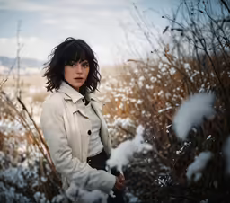 woman standing in the snow in front of bushes
