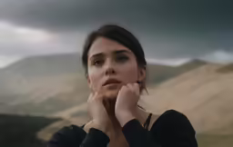 a woman wearing a long sleeved shirt stands in front of mountains