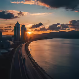 the sun rising behind a city on a street beside water