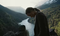 a woman in a brown sweater looks down at the mountains