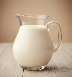 a glass pitcher filled with milk sitting on top of a wooden table