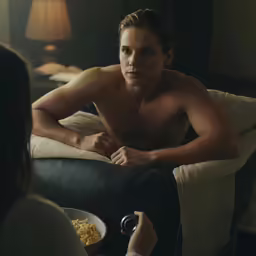 the shirtless man is eating cereal in his room