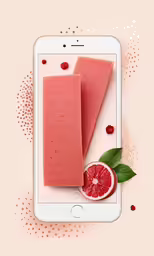 a cell phone with two pink sponges next to a grapefruit