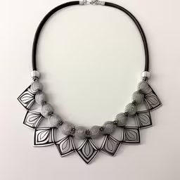 a black leather necklace with silver details,the necklace is made with metal beads,the black and white necklace is displayed on a white surface,the silver necklace is decorated with black and white accents,a metal necklace on a leather cord