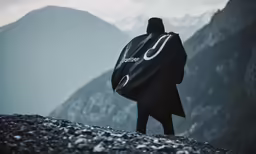 a person is standing with a coat over their head and looking at the mountains