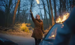 a woman wearing a long brown coat holding up a light bulb above her head
