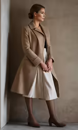 woman standing in front of a wall wearing a tan coat