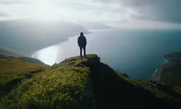 a person stands on the edge of a cliff overlooking water