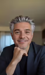 a man with a black suit smiles at the camera