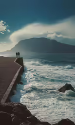 two people stand on the ocean wall near the waves