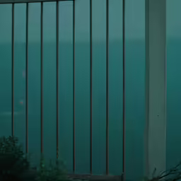 the metal bars of a fence are reflected in a blue pool