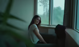 the girl sitting on the couch in the room looks out the window