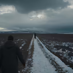 two people in jackets walking down the dirt road