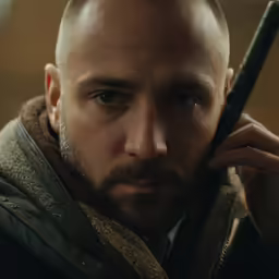a man with a shaved head has an old - fashioned sword on his shoulder